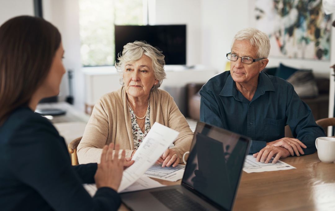 An advisor going over paperwork with an older couple at their dining table.
